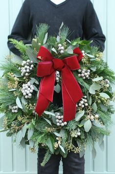 a person holding a wreath with holly and berries