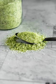 a spoon full of green powder sitting on top of a counter next to a jar