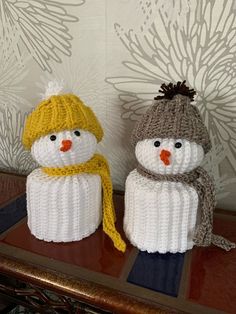 two knitted snowmen sitting next to each other on top of a wooden table