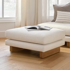 a white ottoman sitting on top of a hard wood floor next to a large window