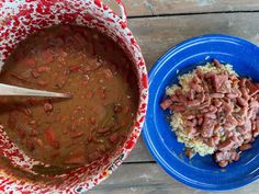 a bowl of beans and rice next to a blue plate on a wooden table with a spoon in it