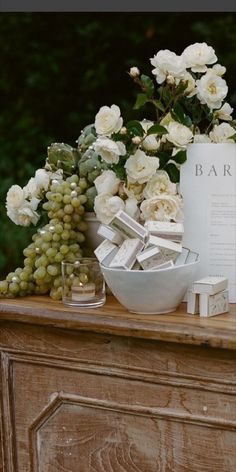 a table topped with white flowers next to a vase filled with grapes and other items