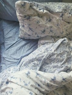 an unmade bed with blue and white flowers on the comforter, pillows and sheets