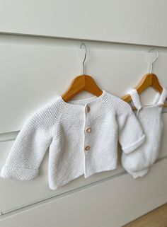 two knitted sweaters hanging on the wall next to each other, with wooden hangers