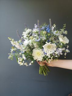 a person holding a bouquet of white and blue flowers in their hand, against a gray background