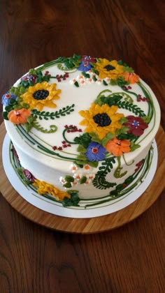 a white cake decorated with sunflowers and leaves on a wooden platter sitting on a table