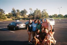 a group of people posing for a photo in a parking lot with cars behind them