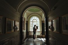 a man and woman are standing in an arched hallway with paintings on the wall behind them