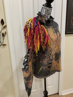 an old mannequin is covered in colorful yarns and metal wire, with a black top hat on it's head