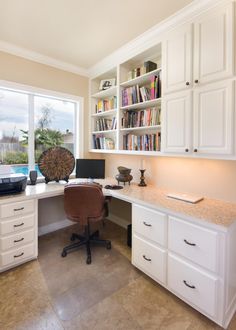 a home office with white cabinets and marble counter tops, along with a large window