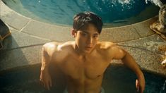 a shirtless young man sitting next to a swimming pool