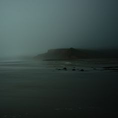 a foggy day at the beach with an island in the distance