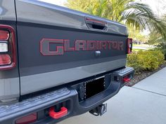 the back end of a gray truck parked in front of a palm tree and bushes