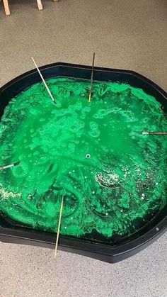 a black tray filled with green liquid and sticks sticking out of the top of it