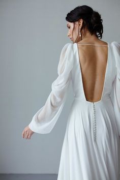 the back of a woman's white dress with long sleeves and beaded necklace