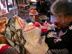 an older woman is knitting at a table full of knits and crochets