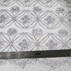 a ruler is next to a white fabric with silver sequins and beads on it