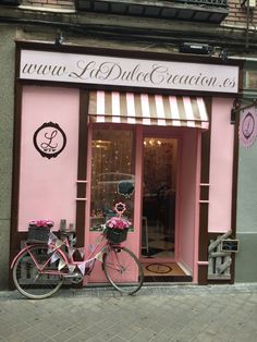 a pink bike is parked in front of a storefront with flowers on the windows