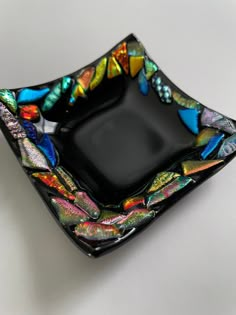 a black glass plate with multicolored butterflies on the edge and bottom, sitting on a white surface