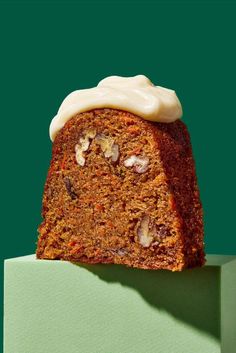 a slice of carrot cake with white frosting on top, sitting on a green surface