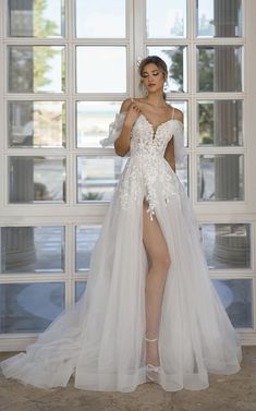 a woman standing in front of a window wearing a white dress with high slits