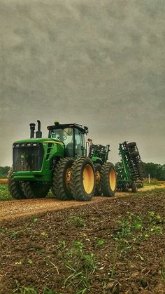 two large tractors are parked on the side of a dirt road in front of a cloudy sky