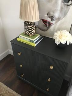 a black dresser with two books and a lamp on top of it next to a painting