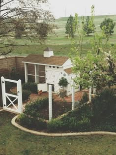 a small white house in the middle of a grassy area with trees and bushes around it