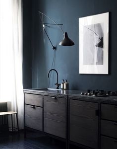 a kitchen with dark blue walls and wooden cabinets, an art work hanging on the wall