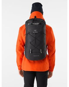 a man in an orange jacket and black hat is looking down at the back of his backpack