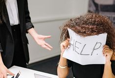 a woman sitting at a desk with a sign on her head that says help above her head