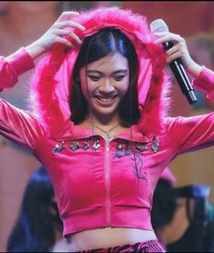 a woman wearing a pink jacket and holding a microphone in front of her head with both hands