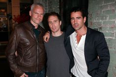 three men standing next to each other in front of a brick wall at night time