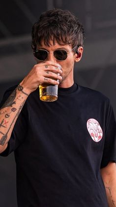 a man drinking from a beer glass while standing next to a stage with tattoos on his arm