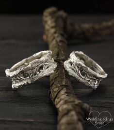 two silver rings sitting on top of a piece of driftwood next to a twig