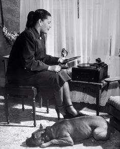 a woman sitting in a chair next to a dog and an old typewriter on a table