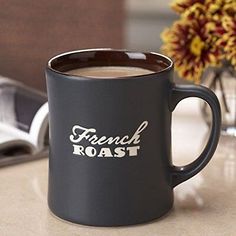 a black coffee mug sitting on top of a counter next to a vase with flowers