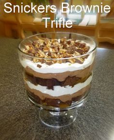 a dessert in a glass dish on a table with the words snickkers brownie trifle