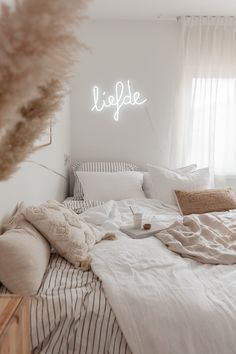 a bed with white sheets and pillows in a bedroom next to a window that reads life