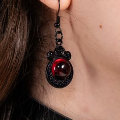 A pair of Gothic earrings adorned with a 1.5 inch tall and 1 inch wide skull made of black painted alloy, accented with a blood red ruby. Black Single Earring For Halloween, Red Gothic Earrings For Pierced Ears, Gothic Black Single Earring, Black Enamel Drop Earrings, Gothic Black Drop Earrings, Gothic Red Nickel-free Earrings, Handmade Black Vampire Earrings, Edgy Red Earrings As Gift, Edgy Red Earrings For Gift