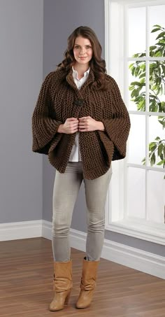 a woman standing in front of a window wearing a brown knitted ponchy