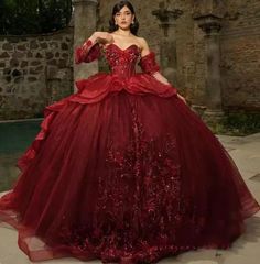 a woman wearing a red dress standing in front of a stone wall with her hands on her hips