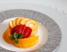 a white plate topped with sliced fruit on top of a silver platter next to a knife and fork