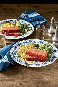 two plates filled with meat and vegetables on top of a wooden table next to silverware