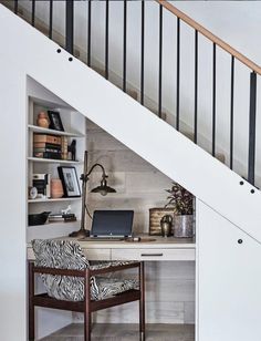 a desk with a laptop on it under a stair case in a home office area