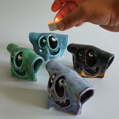 a hand holding a lit lighter over three small ceramic objects with eyes and mouths on them