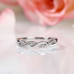 a white gold wedding band with three diamonds on it and a rose in the background