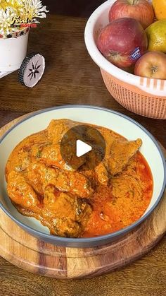 a bowl filled with meat covered in sauce next to bowls of apples and oranges