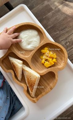 a child's hand is reaching for some food on a tray that includes grilled cheese, fruit and yogurt