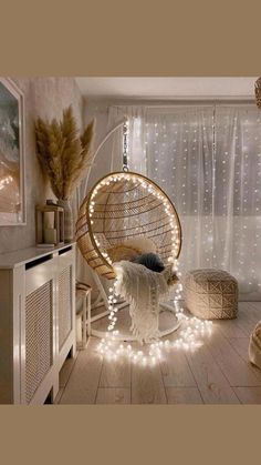 a hanging chair with lights around it in a room that has white curtains and wooden floors